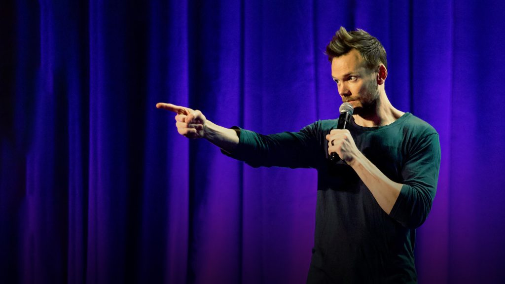 A still image of Joel McHale from his stand-up comedy special, Live From Pyongyang.