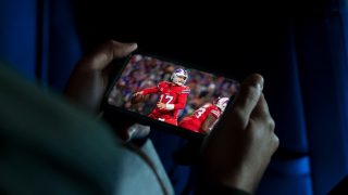 A person holding their phone to stream an NFL game live on Hulu.