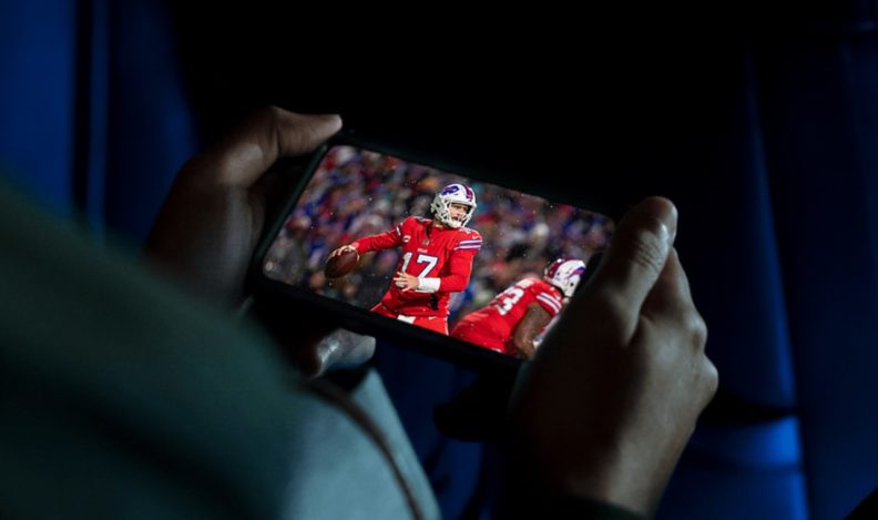 A person holding their phone to stream an NFL game live on Hulu.