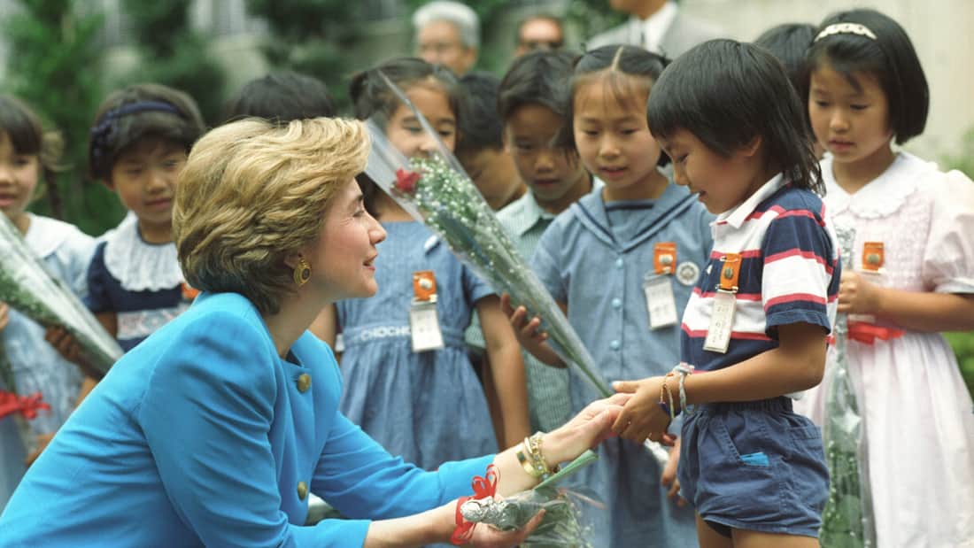 Hillary Clinton kneeling down shaking a young boy’s hand